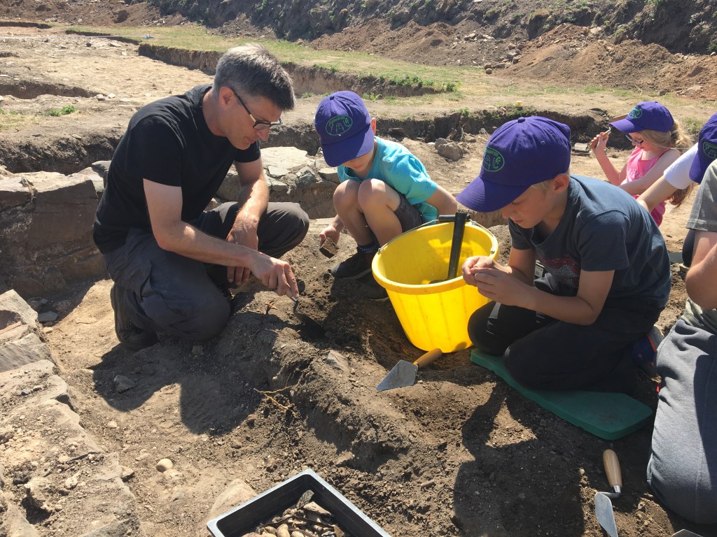 Children excavating soil under the supervision of an adult archaeologist at a post-medieval stable block in Bradgate Park.